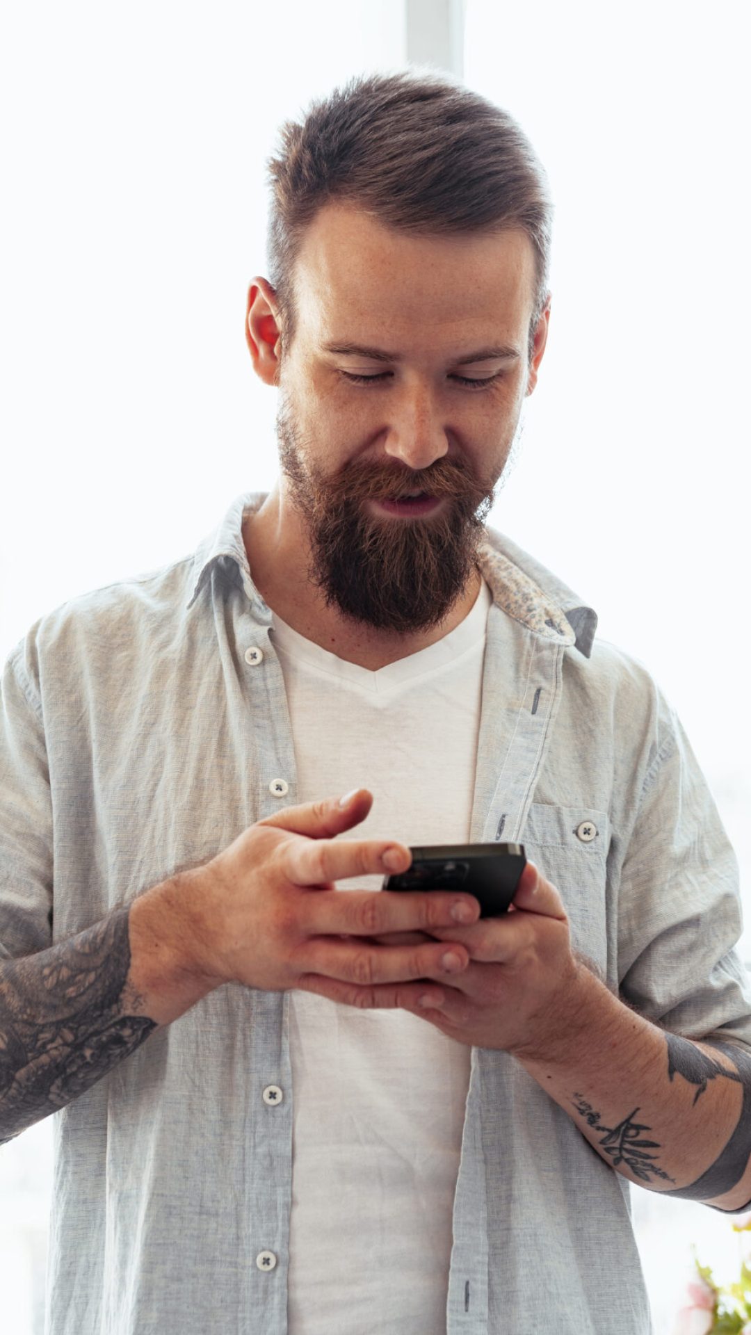 Handsome young bearded man spending time at home with phone in hands close up